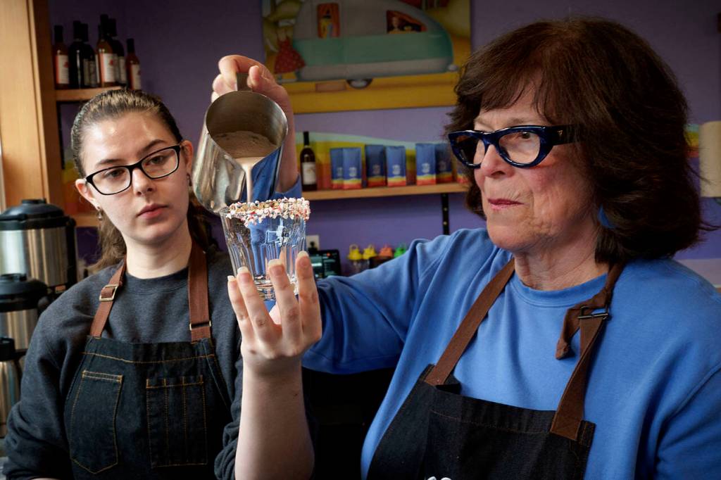 (Photo by David Welton)
Barista Lizzy Taylor holds a glass with a peppermint rim while Dawn Pinaud pours in hot chocolate.