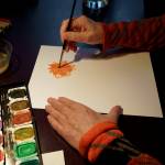 (Photos by David Welton)
Using watercolors, Linda Beeman paints an orange dahlia.