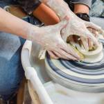 Whidbey Clay Center instructor Jordan Jones helps a student avoid a wobble disaster as she learns the first steps to throwing clay during her class. (Patricia Guthrie / Special to The Herald)