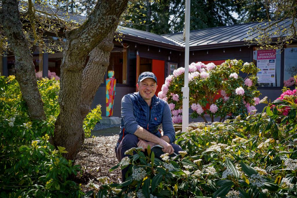 Clinton Community Hall President Mike Gerhardt poses near an old nurse log that members of the South Whidbey Garden Club dragged uphill in the late 1960s. (Photo by David Welton)