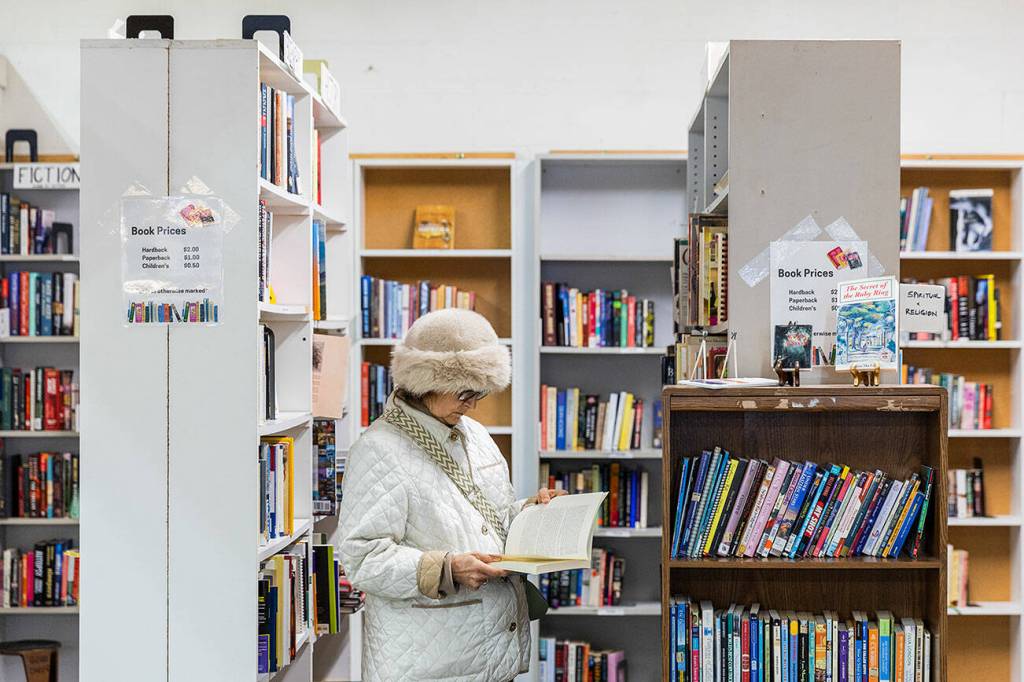 A woman flips through a book at the Good Cheer Thrift Store in Langley. (Olivia Vanni / The Herald)