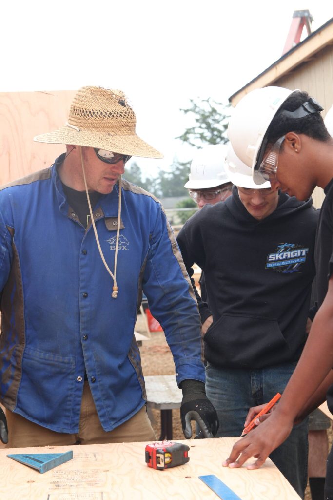 Chris Whiteman helps his students measure the size of their wood panel.