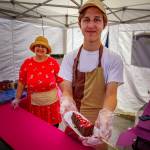 (Photo by David Welton) New vendors Natalia Yamkus and Misha Vilchitsky from Grays Harbor County sell wedges of cheesecake dipped in chocolate and other toppings.