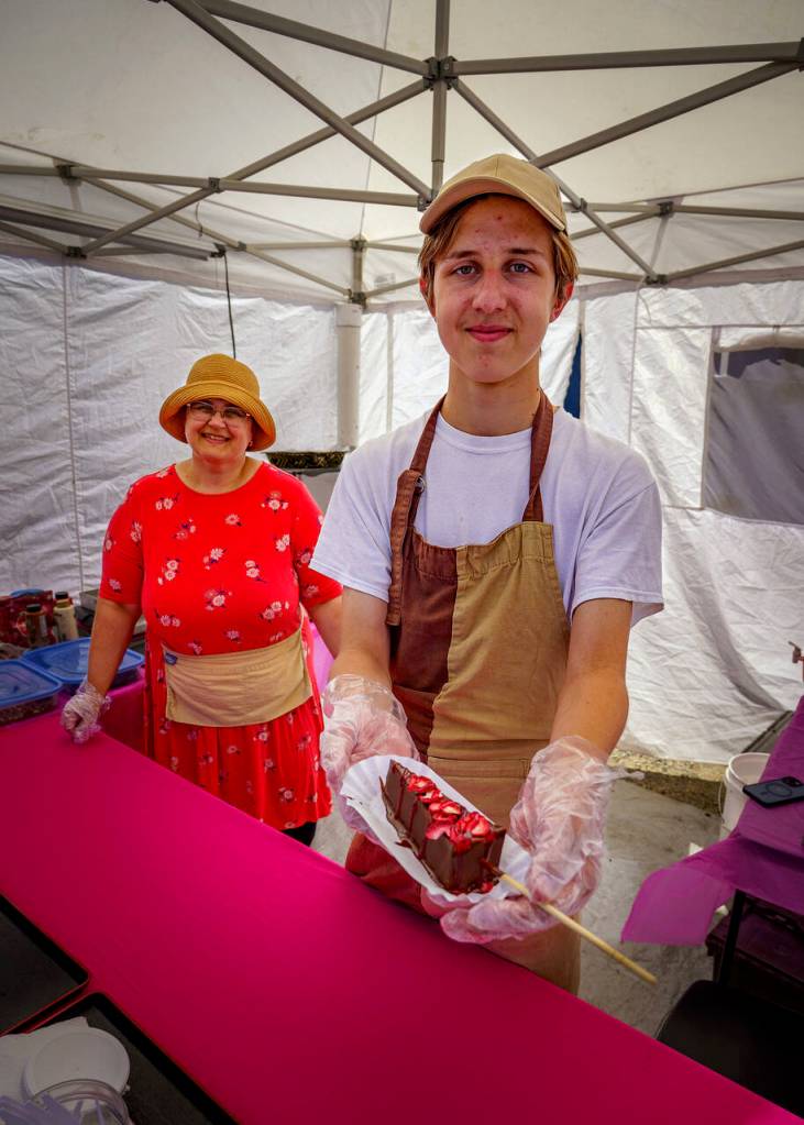 (Photo by David Welton) New vendors Natalia Yamkus and Misha Vilchitsky from Grays Harbor County sell wedges of cheesecake dipped in chocolate and other toppings.