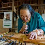 (Photo by David Welton) Sampa Lhundup works on a carving of a Tibetan bird in his studio. A sign in the background proudly proclaims him as the carver of the Dalai Lamas teaching throne.