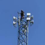 Astound technician installing fixed wireless network transmission devices atop existing headend tower.