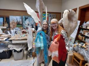 Holly Koteen-Soulé, left, and Melissa Koch with the heads of two puppets that will be part of the Festival of the Elements event. Behind them is a papier-mâché sculpture created by Kochs son-in-law. (Photo by Kira Erickson/South Whidbey Record)
