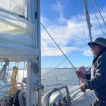 (Photo by Marina Blatt) Bill Smith pulled up the sail as a rainbow peaked through the clouds behind him.
