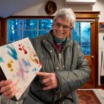 (Photo by David Welton) Jan Naud holds up a painting created by Olive the baboon. Like the artwork, Nauds stories about her time as a wild animal trainer are vivid and colorful.