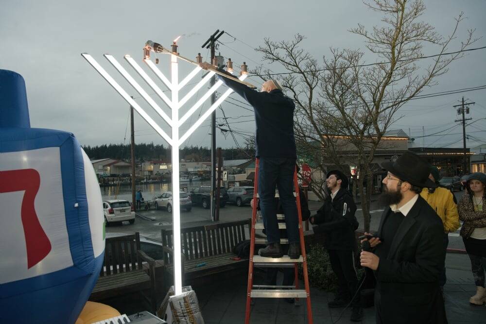 (Photo provided by the Chabad Jewish Center of Skagit County) A man lights the giant menorah, standing on a ladder to reach the candles in last years Hanukkah celebration.